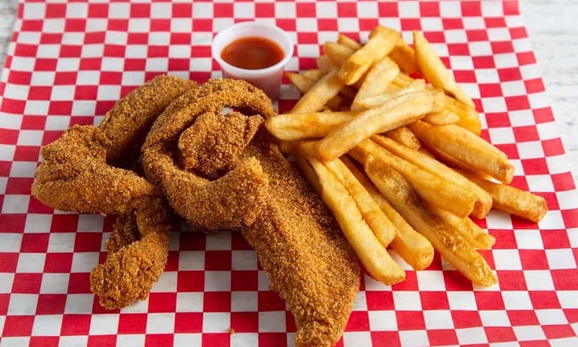 Crispy fried fish fillets and golden french fries served with a side of sauce on red and white checkered paper.